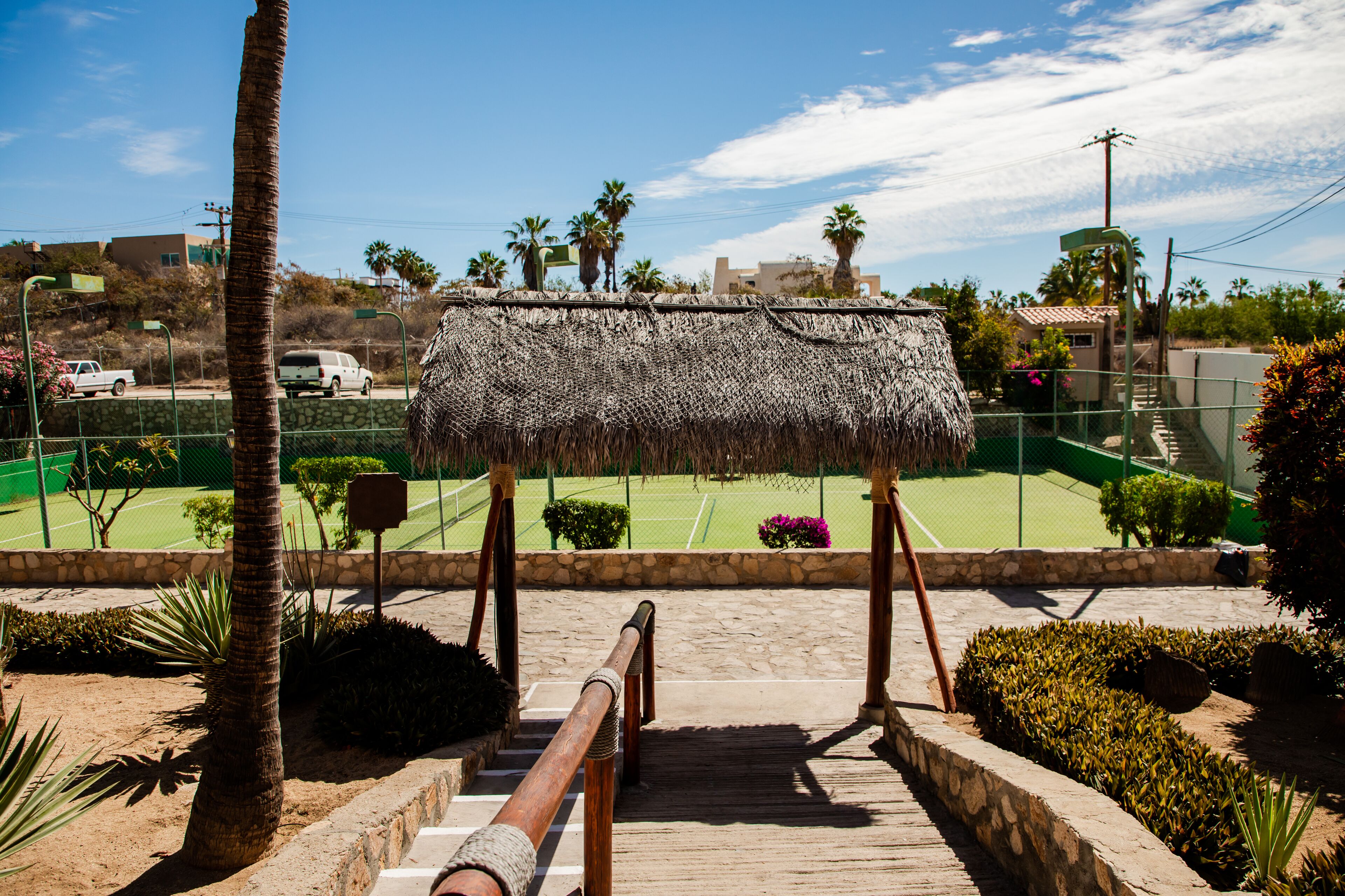 A staircase leading to a thatched-roof structure with a tennis court in the background.