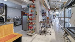 Een schone, moderne keuken met roestvrijstalen apparatuur, een glazen vitrine met snacks en een zithoek met metalen stoelen.