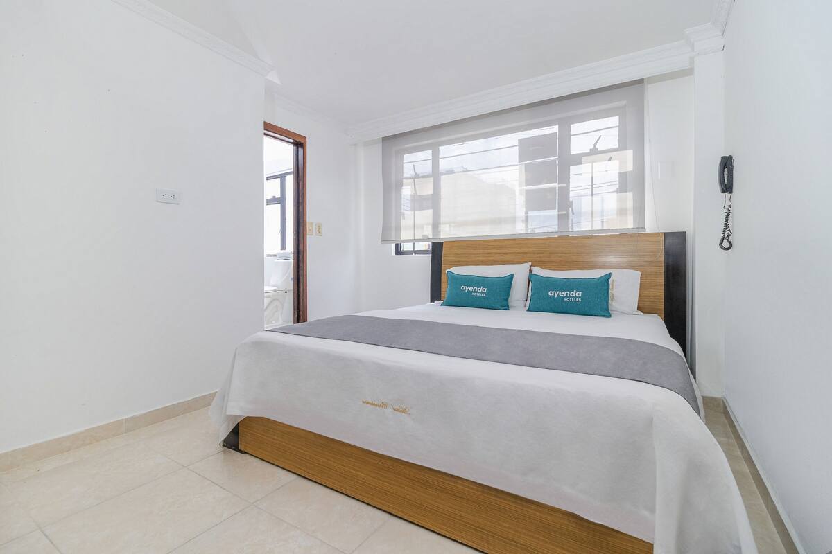 A hotel room with a bed, a window, and a telephone on the wall.