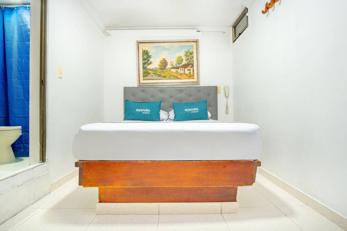 A bedroom with a bed, a painting on the wall, and a bathroom visible through an open door.