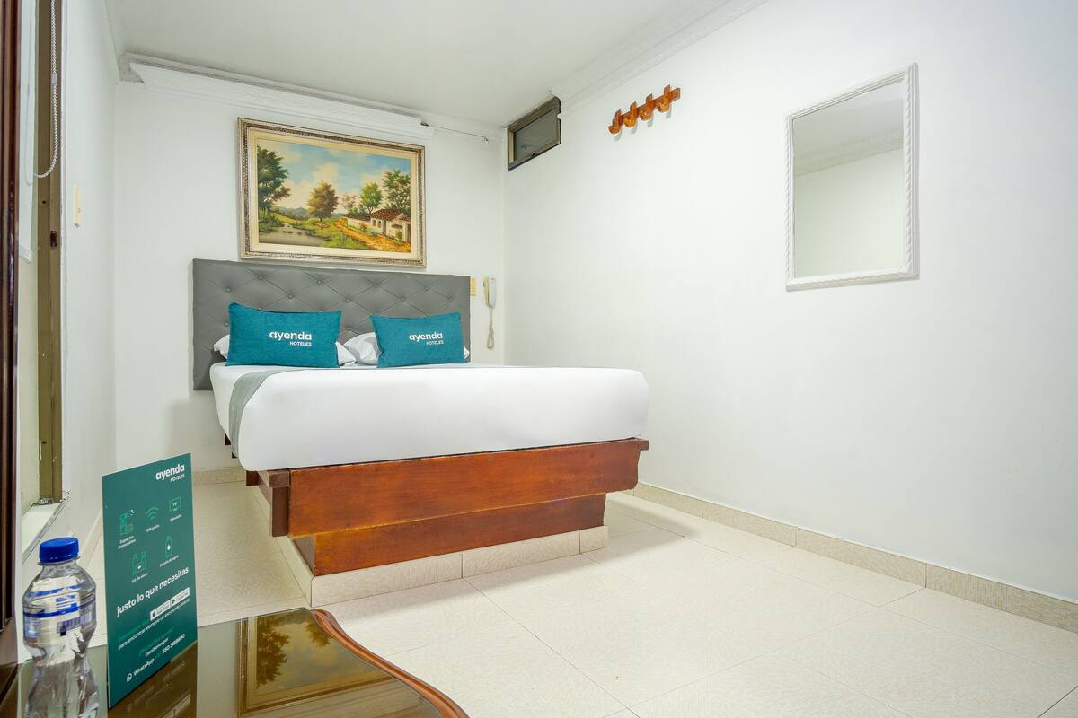 A hotel room with a bed, a painting on the wall, a mirror, and a sign with hotel information.