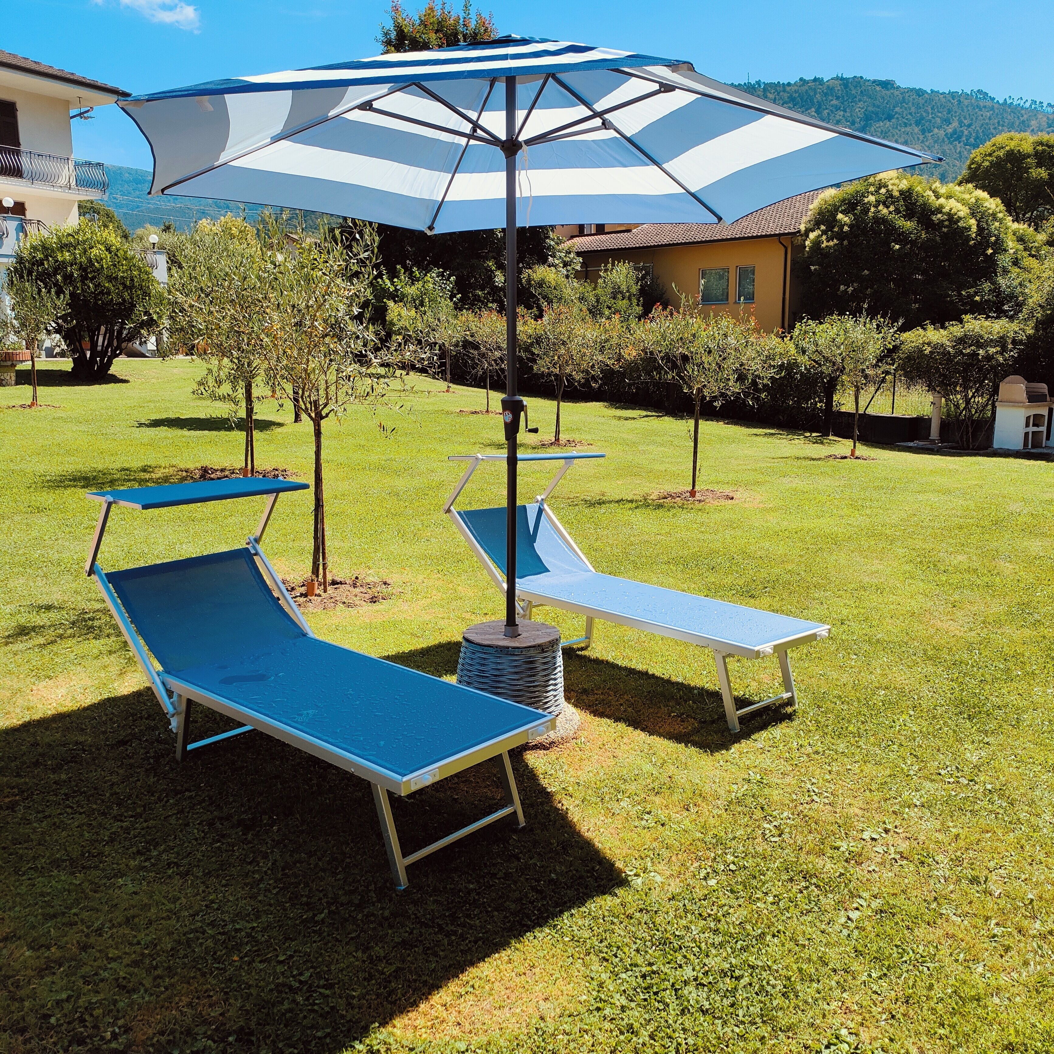 A grassy outdoor area with two blue lounge chairs and a large striped umbrella.
