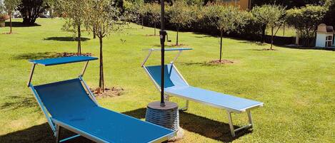 A grassy outdoor area with two blue lounge chairs and a large striped umbrella.