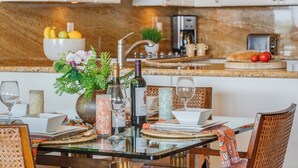 Une cuisine moderne avec un plan de travail en marbre, une table à manger dressée avec des assiettes, des verres et un vase rempli de fleurs.