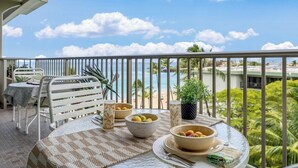 Un balcon avec une table dressée pour un repas, donnant sur une plage et des palmiers.