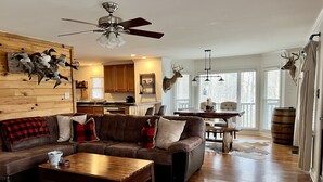 A spacious living room with a wooden floor, a brown leather sofa, a wooden coffee table, and a ceiling fan. - Canvasback Cabin - 2bd/2ba (Scottsboro)