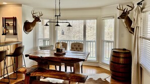 A dining area with a wooden table, chairs, and a bench. There are deer heads mounted on the walls. - Canvasback Cabin - 2bd/2ba (Scottsboro)