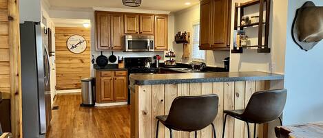 Una cocina moderna con gabinetes de madera, un refrigerador de acero inoxidable, un microondas y una zona de bar con taburetes.