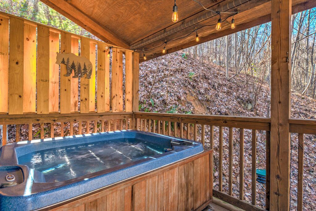 A wooden deck with a hot tub, surrounded by a wooden fence with a bear cutout, and a view of a wooded area.