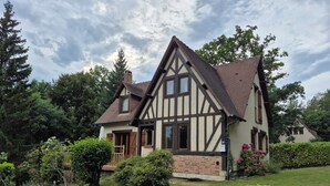 Una casa tradizionale a graticcio con un giardino curato, un camino ben visibile e un vialetto lastricato che conduce all'ingresso.
