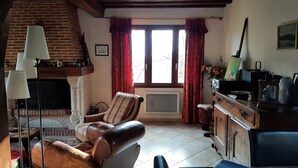 Ein gemütliches Wohnzimmer mit Kamin, einem gestreiften Sessel, einer Couch, einem Holzschrank und einer Heizung.