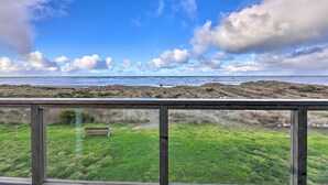 A coastal view from a wooden deck with a bench, grassy area, and rocky terrain. - Sanderling Sea Cottages, Unit 7 w/ Beach Access! (Waldport)