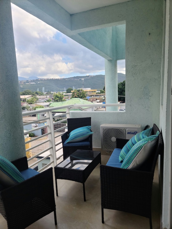 A balcony with wicker furniture, a fan, and a view of a cityscape and mountains.