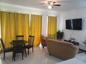 A living room with a sofa, a TV, a ceiling fan, and yellow curtains.