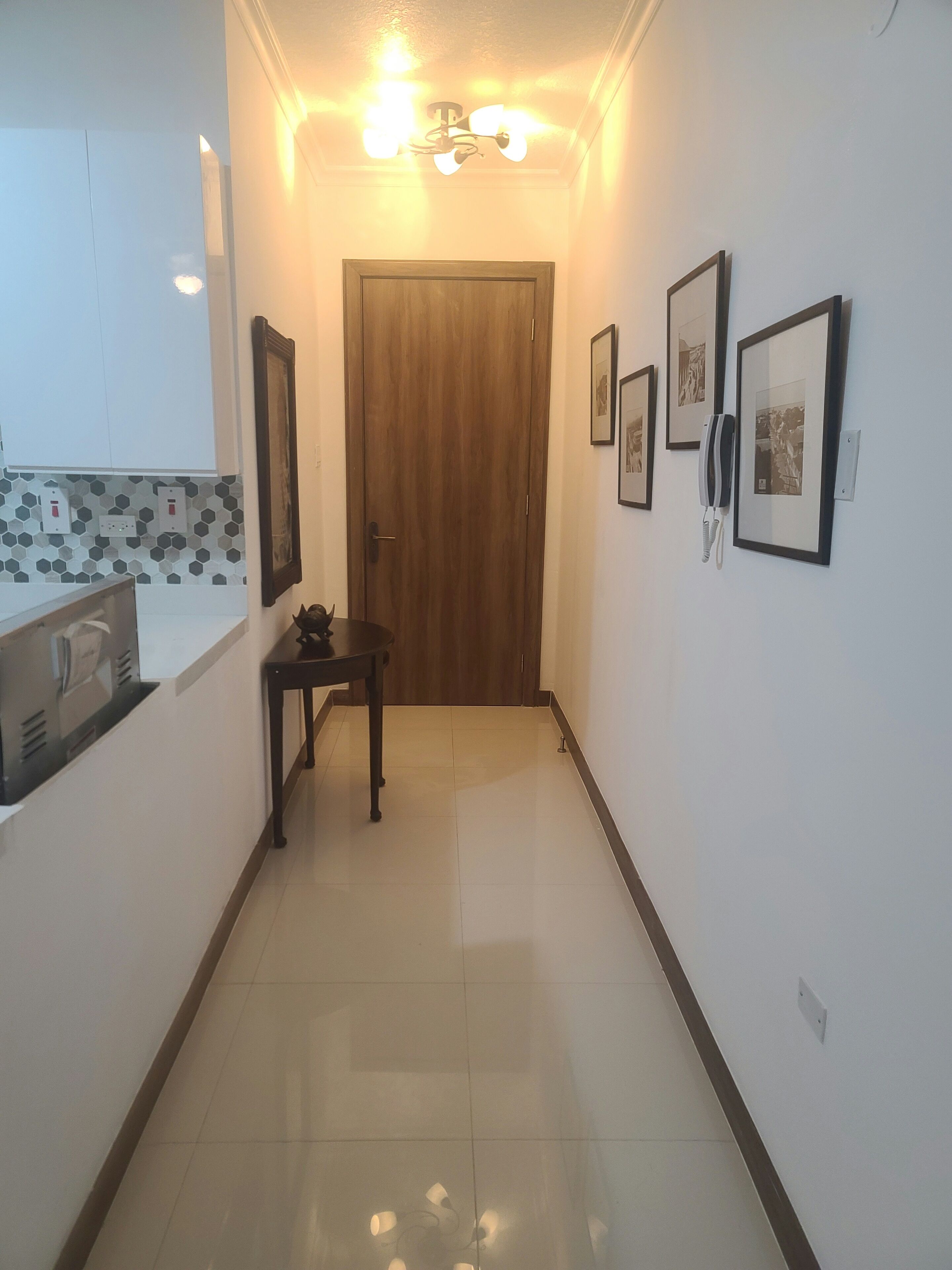 A hallway with a wooden door, framed pictures on the wall, and a small table with a telephone.