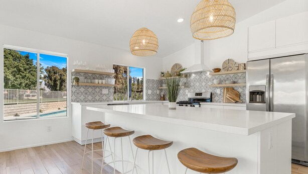 Una cocina moderna con una isla grande, taburetes de bar, lámparas de mimbre colgantes y vistas al exterior.