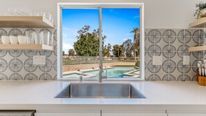 Una cocina con un ventanal que da a una piscina, pileta empotrada y azulejos decorativos en el respuesto.