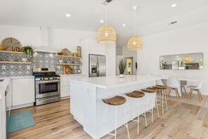 Una cocina moderna con armarios blancos, una isla central con taburetes y una zona de comedor con un espejo grande.
