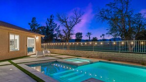 Una piscina con un borde de baldosas, un patio con sillas y una valla con luces.
