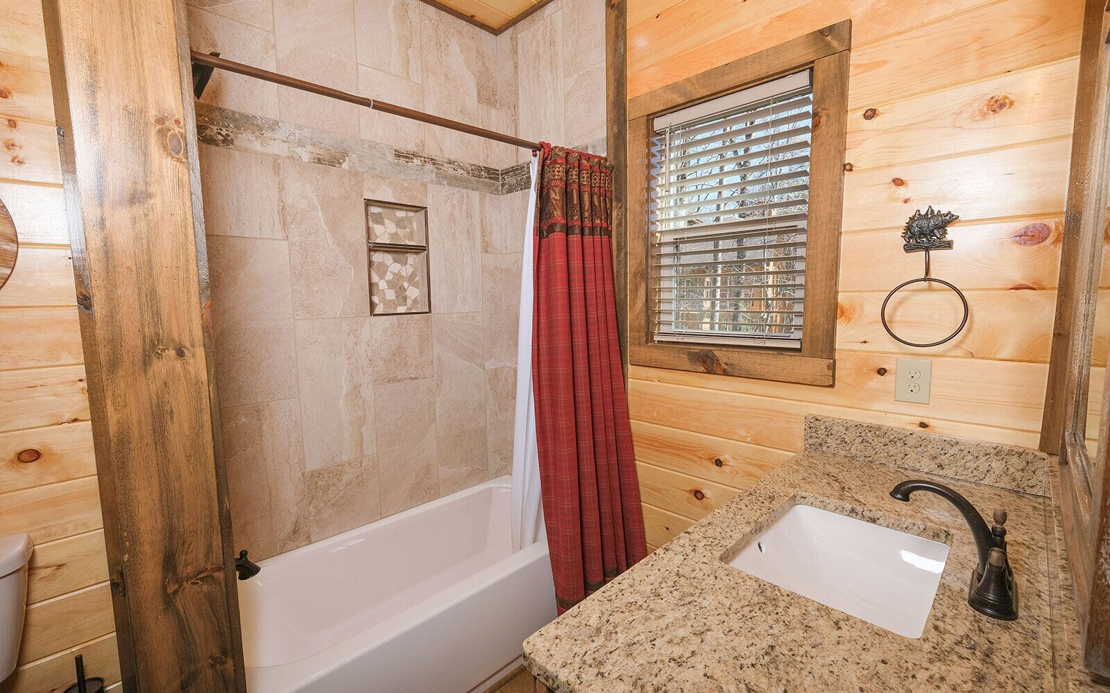 A wooden cabin bathroom with a bathtub, a window with blinds, a sink, and a towel ring.
