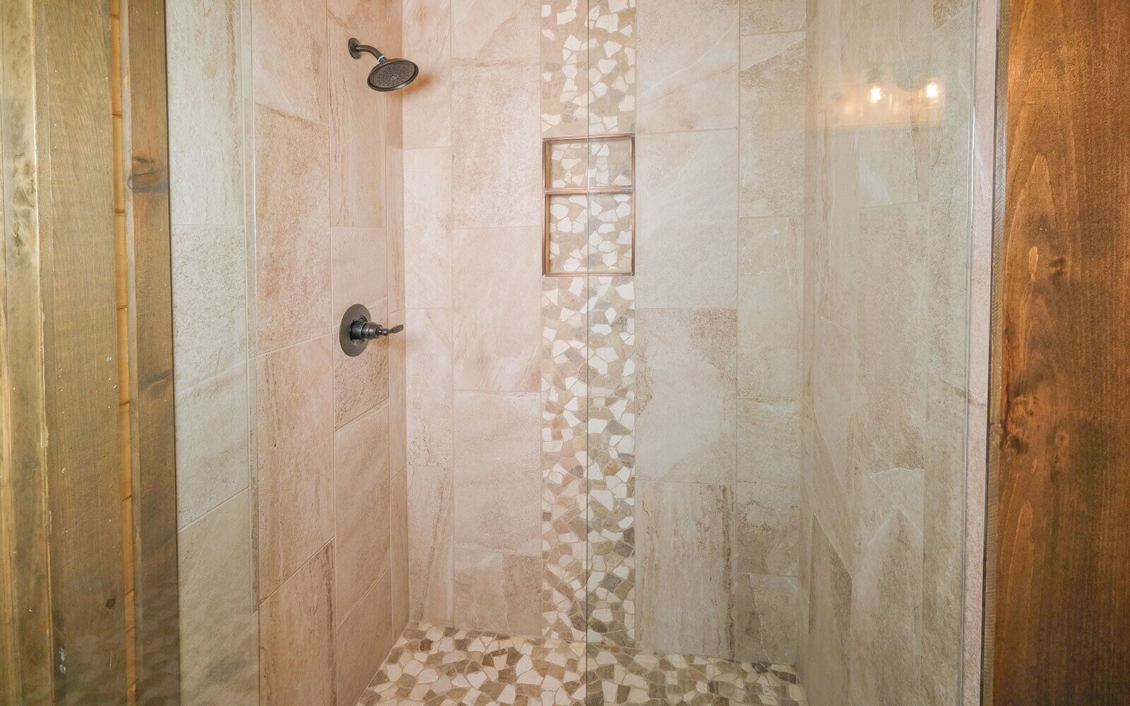 A shower with a tiled wall, a showerhead, and a control knob.