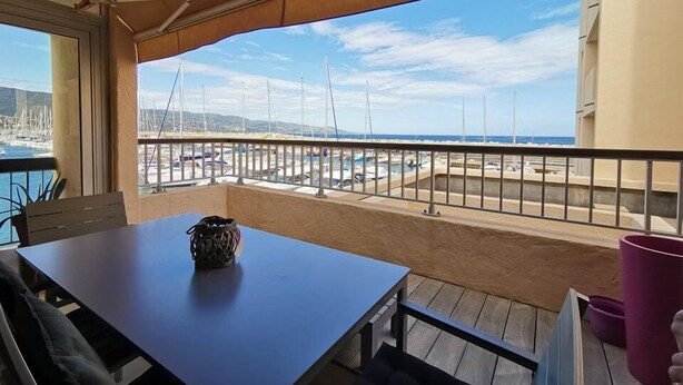 A balcony with a view of the marina and boats, a table with a decorative item, and a purple container. - Rental of a 2 rooms apartment, for up to 4 persons, in a residence with a pool, in the La... (BORMES LES MIMOSAS)