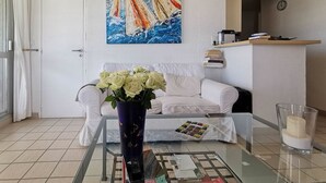 A living room with a white sofa, a glass coffee table, a vase with flowers, a painting of sailboats, and a clock on the wall. - Rental of a 2 rooms apartment, for up to 4 persons, in a residence with a pool, in the La... (BORMES LES MIMOSAS)
