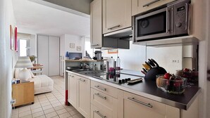 A modern kitchen with a microwave, stove, and various kitchen utensils. There is a dining area with a table and chairs visible in the background. - Rental of a 2 rooms apartment, for up to 4 persons, in a residence with a pool, in the La... (BORMES LES MIMOSAS)