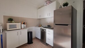 Una cocina compacta con armarios blancos, un refrigerador de acero inoxidable, un microondas y un lavavajillas.