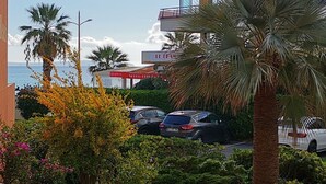 Un edificio de varios pisos con balcones, coches aparcados y palmeras.