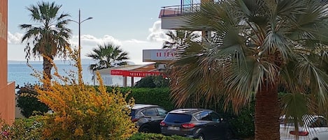 Un edificio de varios pisos con balcones, coches aparcados y palmeras.