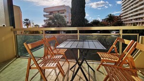 Un balcón con mesa y sillas, con vistas a un edificio y palmeras.