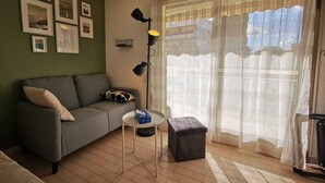 Una sala de estar con un sofá, una mesita redonda, un otoman negro y una pared decorada con cuadros.