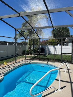 Une piscine entourée d’une rampe de sécurité en métal, bordée d’une terrasse couverte d’où l’on peut admirer un quartier résidentiel.