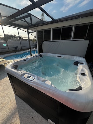 Un bain à remous doté d’un panneau de commande, situé à côté d’une piscine et abrité sous une structure couverte.