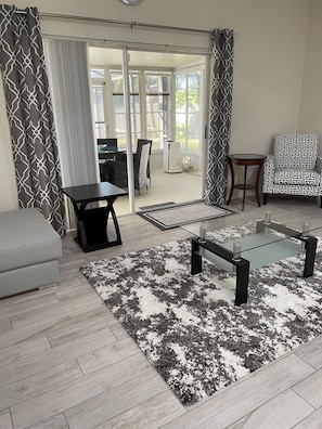 Relax in this stylish living room with a sofa, armchair, and patterned rug, offering ample seating and a sliding glass door to an outdoor area.