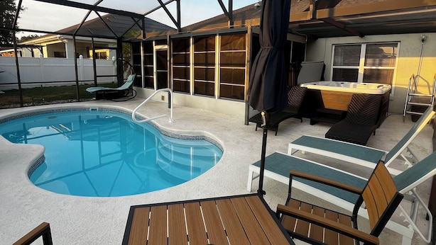 Ein überdachter Außenbereich mit Pool, Liegestühlen und einem Tisch.