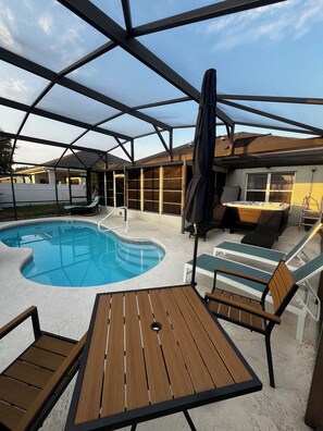 Un espacio al aire libre cubierto con piscina, sillas de descanso y una mesa.