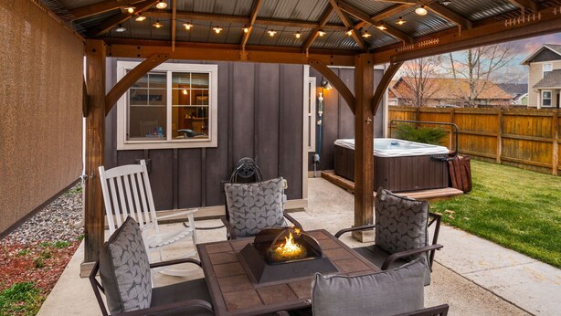 An outdoor patio with a fire pit, wooden furniture, and string lights. - Charming Home by the Park with a Hot Tub (Bozeman)