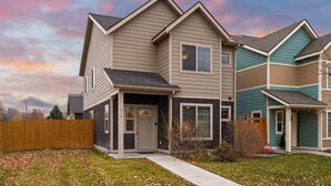 A two-story residential building with a front porch, a garage, and a fenced yard. - Charming Home by the Park with a Hot Tub (Bozeman)