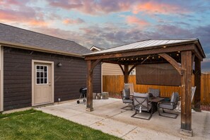 A covered patio with outdoor furniture, a grill, and a wooden pergola with string lights. - Charming Home by the Park with a Hot Tub (Bozeman)