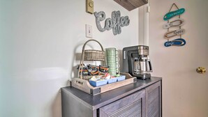 Een koffiehoek met een koffiezetapparaat, een rieten mand en een schaal met koffiekapsules en een mok.