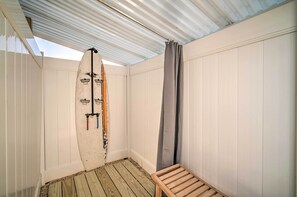 Ein kleiner, abgeschlossener Raum mit Holzboden, einer weißen Wand mit einem Surfbrett und einem grauen Vorhang.