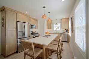 A modern kitchen with wooden cabinets, stainless steel appliances, and a central island with bar stools. - Coastal Brigantine Retreat - Walk to Beach! (Brigantine)