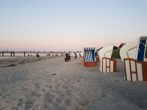 A beach with sand, beach chairs, and a pier in the background.