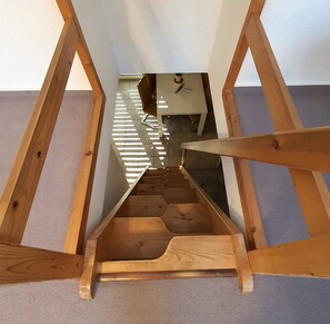 Eine schlichte Holztreppe führt zu einem kleinen Raum mit Schreibtisch und Stuhl.