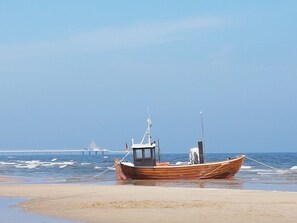Un bote de madera en una playa arenosa, con agua tranquila y un cielo despejado.