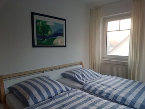A bedroom with a bed, a window with curtains, and a framed picture on the wall.