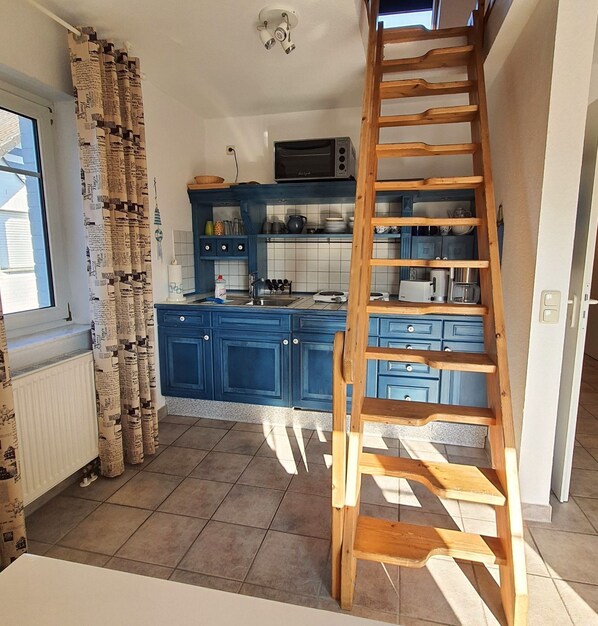 A kitchen with blue cabinets, a wooden ladder, and a microwave.