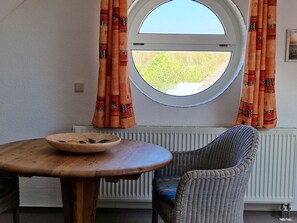 Una habitación con ventanal redondo, una silla de mimbre y una mesa de madera con un cuenco.